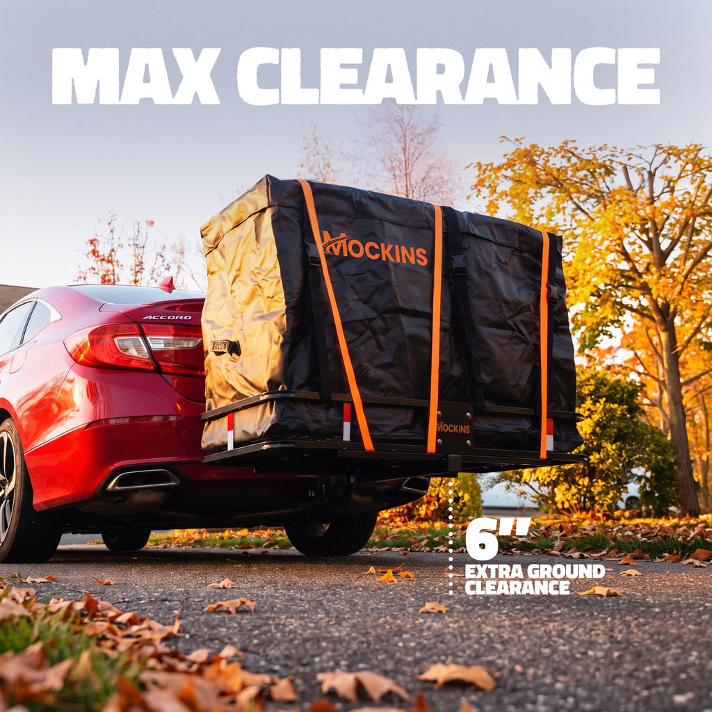A black Mockins cargo carrier cover strapped to the rear of a red car, shown outdoors on a paved road with trees and fallen leaves. Large text at the top reads “MAX CLEARANCE,” and a callout at the bottom right says “6” EXTRA GROUND CLEARANCE.
